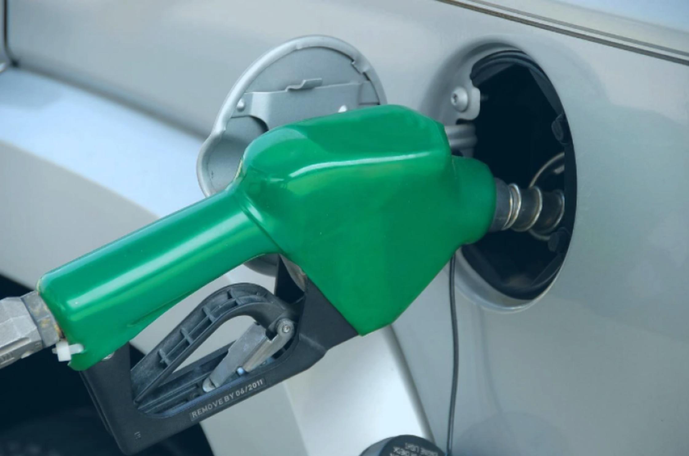 Green gas pump handle with gas pump inserted into white or light grey car